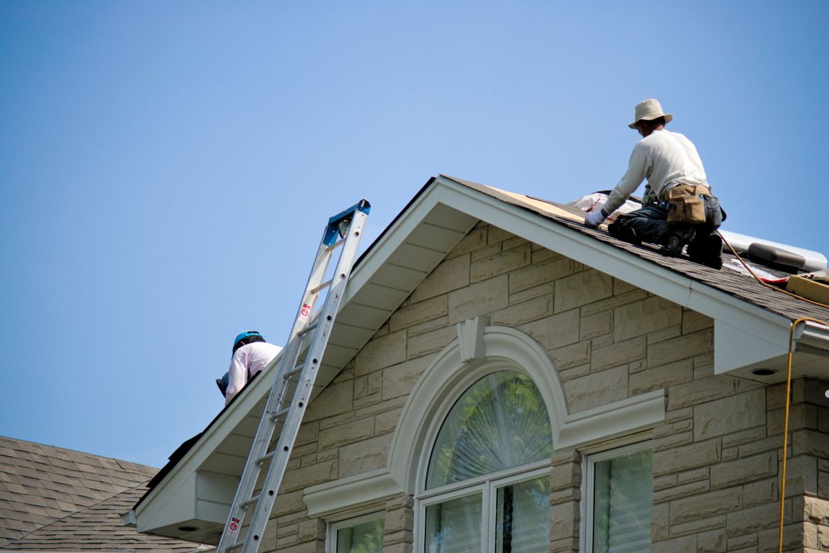 Two men installing flashing and drip edge on the roof of a house, focused on their work and using safety equipment.