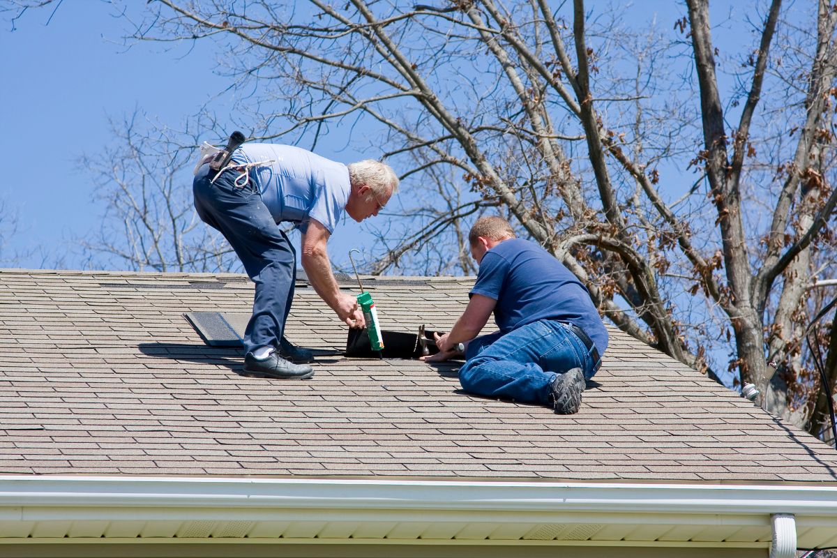 Two men installing roof flashing while using a ladder on a residential roof